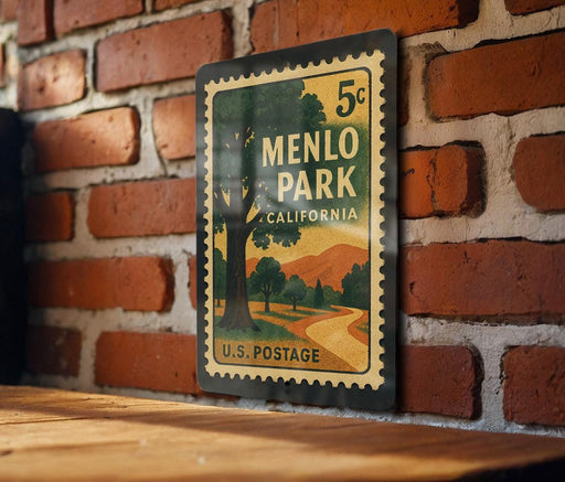 A vintage-style postage stamp from Menlo Park, California, featuring a scenic landscape with a tree and mountains, mounted on a brick wall.