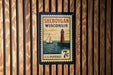 A vintage-style postage stamp from Wisconsin featuring a lighthouse and a sailboat, mounted on a wooden wall.