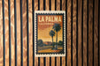 A vintage-style poster of La Palma, California, featuring palm trees and a building, is displayed on a wooden wall.