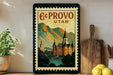 A framed vintage-style poster of a castle or palace, with mountains in the background, is displayed on a wall next to a wooden cutting board and some potted plants.