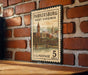 A vintage postage stamp from the United States of America, featuring a cityscape and a bridge, mounted on a brick wall.