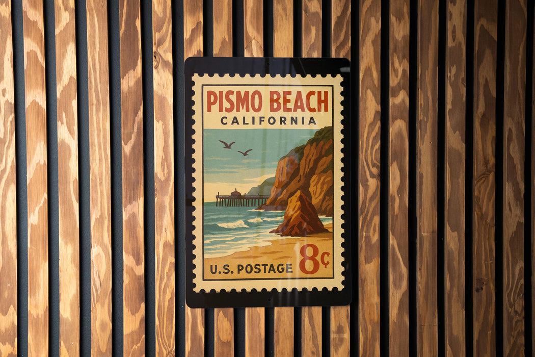 A vintage postage stamp from Pismo Beach, California, featuring a beach scene with a pier and cliffs, mounted on a wooden wall.