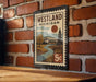 A vintage-style postage stamp from Westland, Michigan, featuring a scenic landscape with a river, trees, and a house.