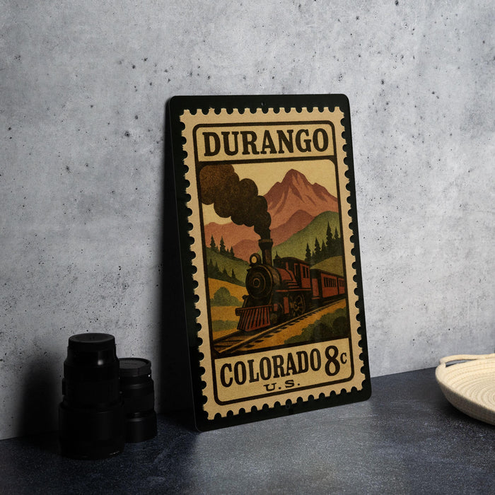 A framed vintage-style postage stamp depicting a train on a mountain, with the text "DURANGO COLORADO 8c" printed on it.