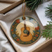 A decorative ornament in the shape of a guitar, with a floral border, is displayed in a box alongside some pine branches.