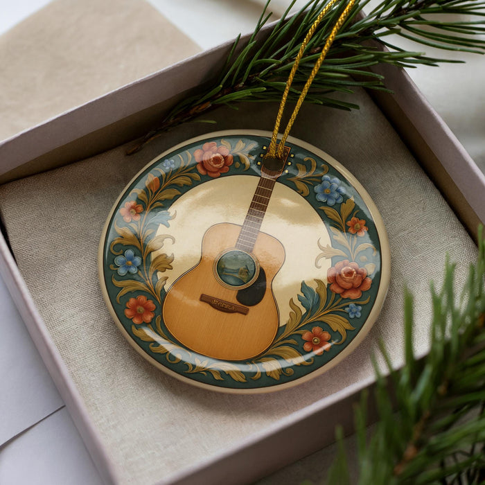 A decorative plate with a guitar design is placed inside a box, surrounded by pine branches.