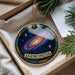 A decorative ornament in a box, featuring a colorful depiction of a galaxy with stars and the word "ANDROMEDA" written on it.