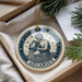 A decorative ornament in the shape of a man pouring water, representing the Aquarius zodiac sign, is displayed on a surface with pine branches and a white card.