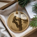 A round ornament featuring a man in a hard hat and safety harness, climbing a tree, is displayed in a box with pine branches and a white card.