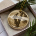 A round ornament featuring a man climbing a tree, with a pine branch and greenery in the background.
