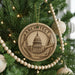 A round ornament on a Christmas tree, featuring an image of the United States Capitol building and various architectural elements.