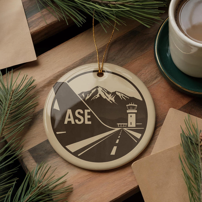 A circular ornament with a graphic design featuring a mountain range and a control tower, along with the word "ASE" prominently displayed.
