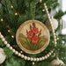 A round ornament with a floral design hangs from a Christmas tree, surrounded by other ornaments and lights.