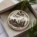 A circular ornament with a graphic of a city skyline and the text "AUB DHABI" is displayed in a box, surrounded by pine branches.