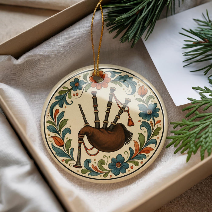 A decorative ornament featuring a piper's bagpipe is displayed in a box, surrounded by pine branches and a white card.