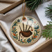 A decorative ornament featuring a piper's bagpipe is displayed in a box, surrounded by pine branches and a white card.