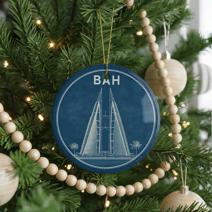 A blue ornament with a drawing of a tall building, surrounded by Christmas lights and ornaments on a decorated Christmas tree.