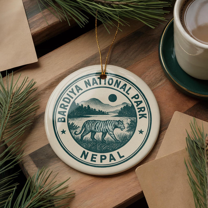 A decorative ornament featuring the text "Bardiya National Park Nepal" and an illustration of a tiger walking through a grassy landscape, surrounded by pine branches and a cup of coffee.