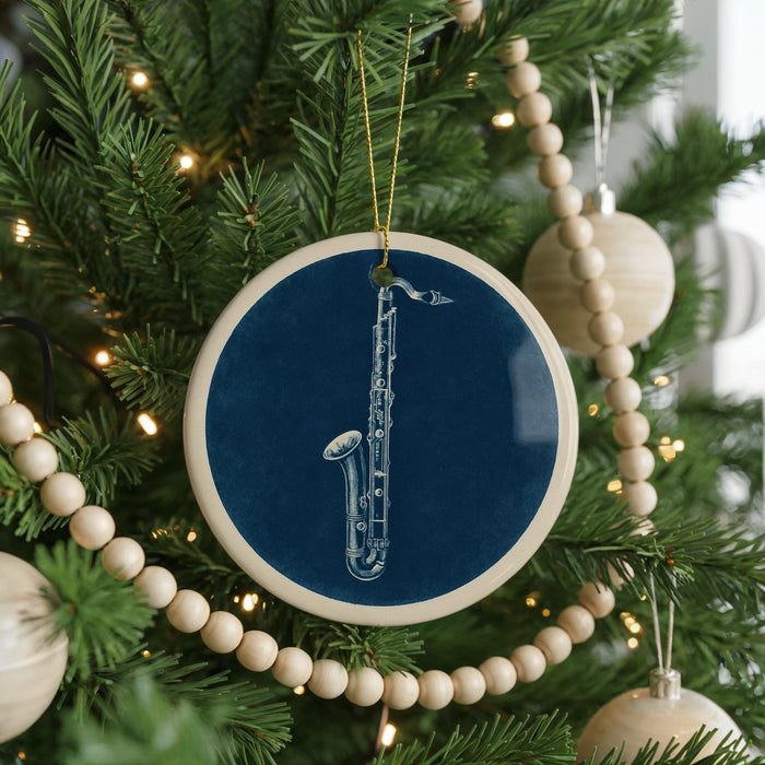 A blue ornament with a white saxophone is hanging on a Christmas tree, surrounded by white beads and greenery.