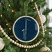 A blue ornament with a white saxophone is hanging on a Christmas tree, surrounded by white beads and greenery.
