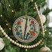 A Christmas tree decorated with ornaments, including a round ornament with a saxophone design and a string of wooden beads.
