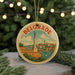 A round ornament with a picture of a monument and a river, surrounded by greenery and a string of lights.