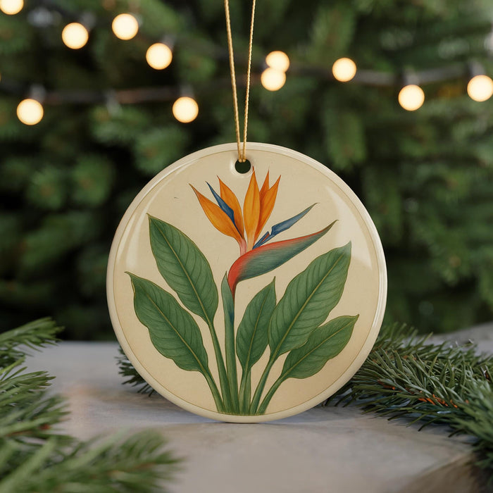 A round ceramic ornament with a floral design featuring a large orange flower surrounded by green leaves, placed on a surface with pine branches in the background.