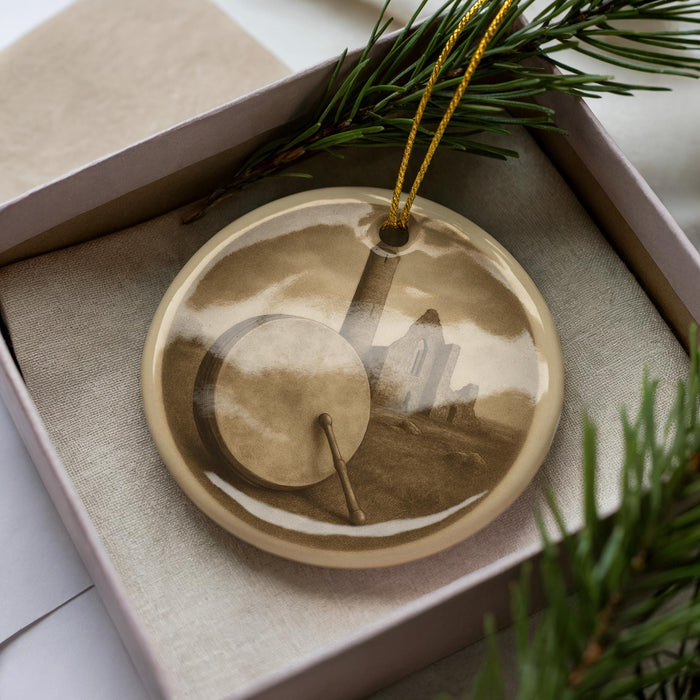A round ornament with a picture of a building and a drum on it, placed in a box with pine branches.