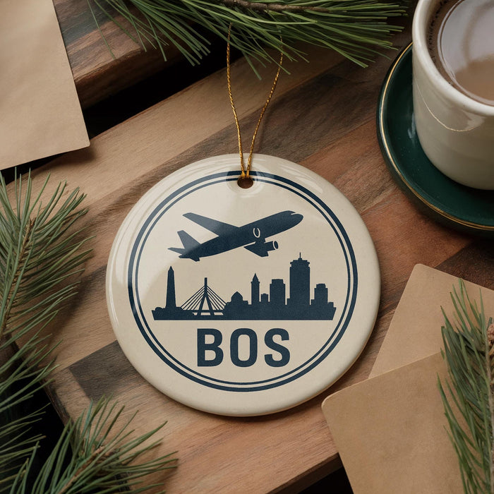 A circular ornament with a silhouette of a city skyline and an airplane, along with the word "BOSTON" written on it, is displayed on a wooden surface.