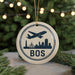 A circular ornament with a silhouette of a city skyline and an airplane, along with the text "BOS" (Boston, Ohio) on it, is displayed on a Christmas tree.