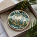 A decorative ornament featuring a cityscape of Calgary, Canada, with a bridge and skyline in the background.