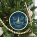 A Christmas tree decorated with ornaments, including a circular ornament featuring a bonfire with chairs around it.
