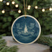 A round ornament featuring a campfire with two camping chairs in front of it, surrounded by pine branches and twinkling lights.