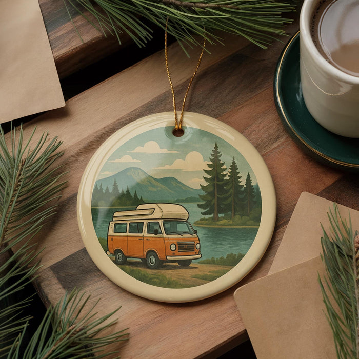 A round ornament featuring an illustration of a camper van on a road, surrounded by pine trees and mountains, with a lake in the background.