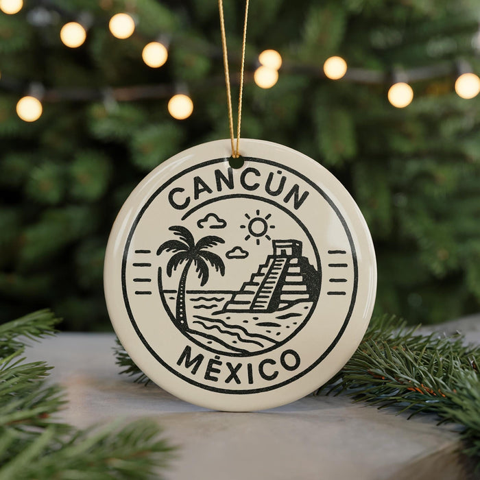 A circular ornament with the text "CANCUN MEXICO" and a graphic of a palm tree and a pyramid, hanging in front of a Christmas tree with lights.
