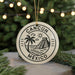 A circular ornament with the text "CANCUN MEXICO" and a graphic of a palm tree and a pyramid, hanging in front of a Christmas tree with lights.