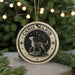 A circular ornament with a dog and stars, surrounded by a decorative border, is displayed in front of a Christmas tree with twinkling lights.