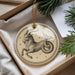 A decorative ornament featuring a stylized depiction of a goat or ram, with stars and a star-like design around it, is displayed in a box with pine branches.