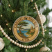 A Christmas tree decorated with ornaments, including a circular ornament with a scenic image of a coastal town and the text "Carmel-by-the-Sea USA".