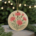 A round ornament with a floral design featuring pink carnations is displayed against a blurred background of a Christmas tree with twinkling lights.