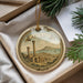 A decorative ornament with a circular design featuring a cityscape and a mountain, hanging from a string.