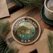 A circular ornament with the text "CATALINA ISLAND U.S.A." and a scenic illustration of Catalina Island, surrounded by pine branches and a cup of coffee.