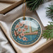 A decorative ornament with a floral design and a tower in the background, placed in a box with pine branches.