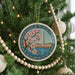 A Christmas tree decorated with ornaments, including a circular ornament featuring a floral design and a tower.