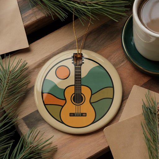 A round ornament featuring a guitar design is placed on a wooden surface, surrounded by pine branches and a cup of coffee.