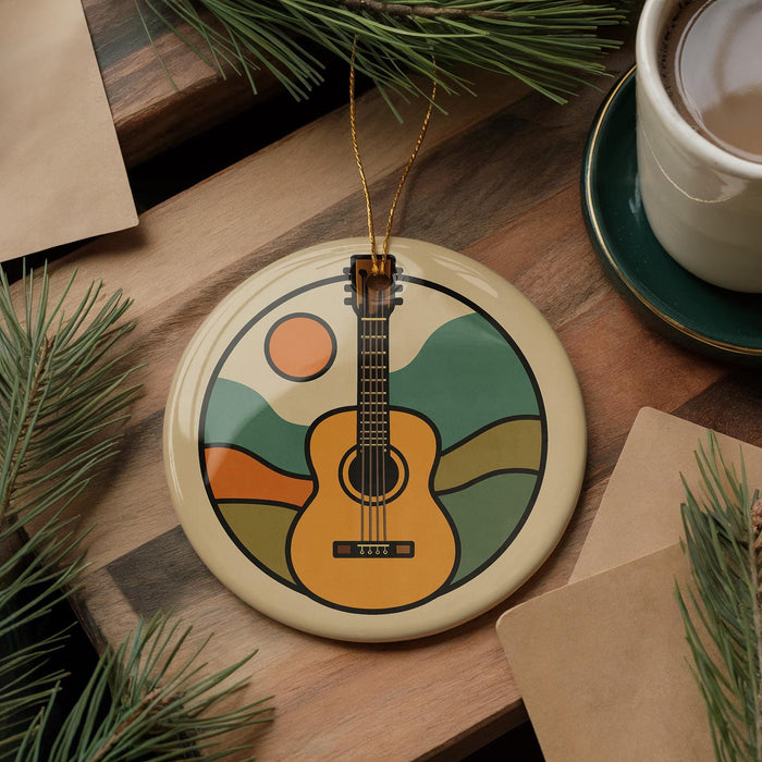 A round ornament featuring a guitar design is placed on a wooden surface, surrounded by pine branches and a cup of coffee.