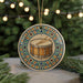 A decorative ornament featuring a drum is displayed on a table, surrounded by pine branches and twinkling lights in the background.