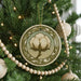 A Christmas tree decorated with ornaments, including a circular ornament with a white cotton flower design.