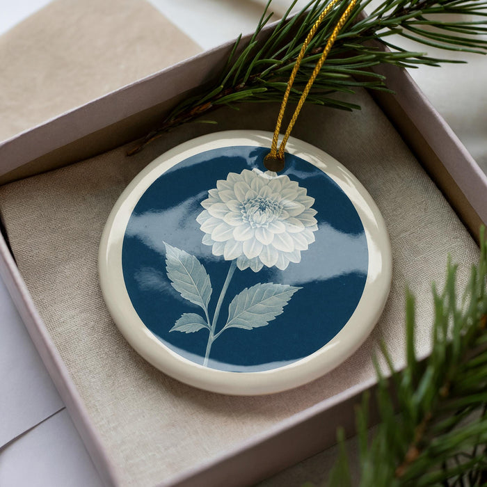 A decorative ceramic ornament with a blue and white floral design, placed in a box with pine branches.