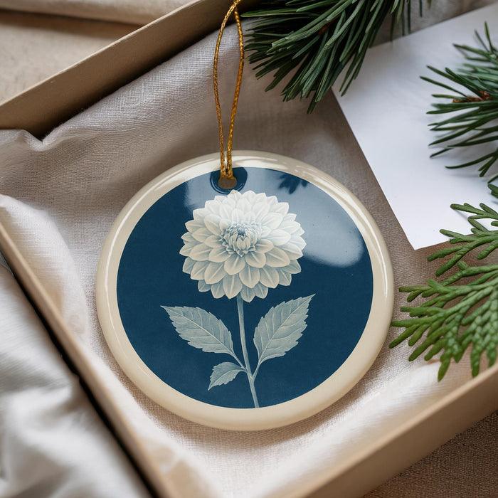 A blue and white ceramic ornament with a white flower design is displayed in a box, surrounded by pine branches and a white card.